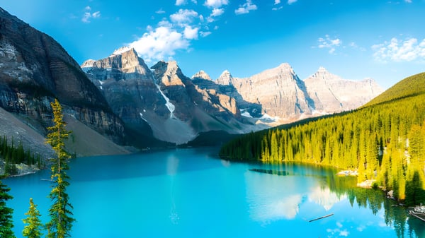 Un tranquilo lago turquesa rodeado de montañas nevadas y bosques verdes cerca de la Robert Thirsk High School.