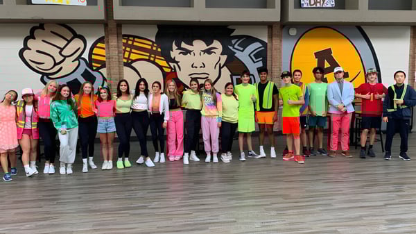 Un grupo de estudiantes está frente a una pared con colorido arte de graffiti en el campus de Rochester Community Schools.