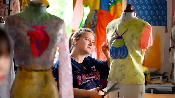 Una estudiante de Rochester Independent College está atenta entre coloridas prendas en un aula de textiles.