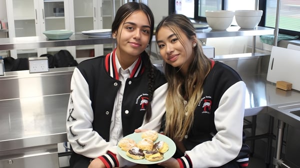 Dos estudiantes de la Rockingham Senior High School están en una cocina sosteniendo un plato con pasteles.