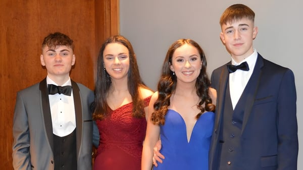 Cuatro estudiantes de la Rockport School posan con ropa formal frente a un fondo de madera.