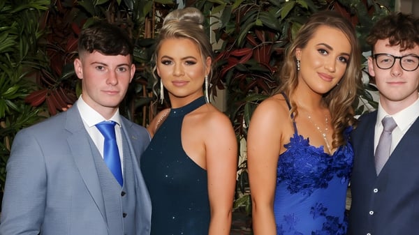 Cuatro personas posan frente a un fondo tropical en el campus del Rockwell College.