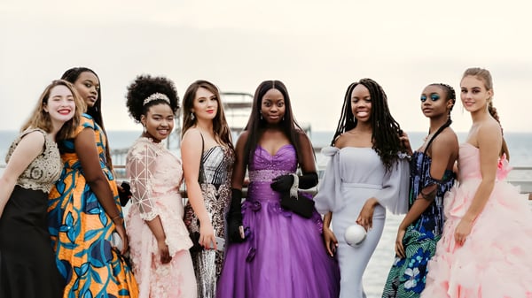 Un grupo diverso de mujeres en vestidos elegantes posan juntas frente a un fondo blanco en la Roedean School.