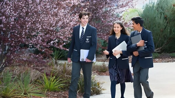 Tres personas están juntas en el jardín frente a flores de cerezo en el terreno del Roma Mitchell Secondary College.