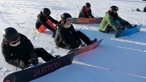 Estudiantes del Roncalli College llevan tablas de snowboard en la pendiente nevada y se preparan para hacer snowboard.