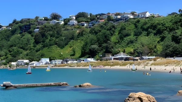 Vista de una ciudad costera con veleros y nadadores en el agua cerca del Rongotai College.