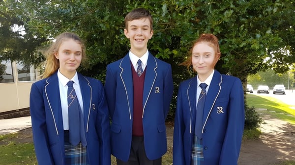 Tres alumnos en uniformes escolares están de pie afuera frente a un prado verde en el terreno de la Rookwood School.