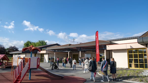 Un grupo de estudiantes está frente al edificio de la Rose-Des-Vents School en el área exterior bajo un cielo azul.