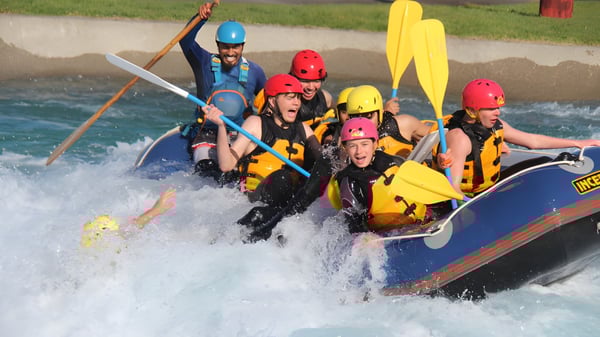 Alumnos del Rosmini College navegan en una balsa a través de un río caudaloso en un paisaje verde.