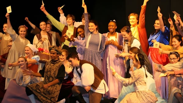 Un grupo de alumnas de la Rothesay Netherwood School celebra en coloridos disfraces con los brazos en alto.