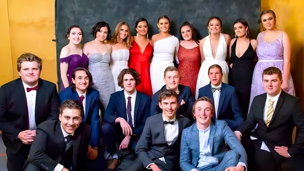 Un grupo de alumnas y alumnos vestidos formalmente posan frente a un fondo amarillo en el campus de la Roxby Downs Area School.