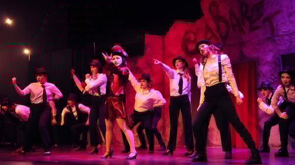 Un grupo de estudiantes de la Royal Bay Secondary School realiza una animada actuación de baile en un escenario con iluminación roja y violeta.