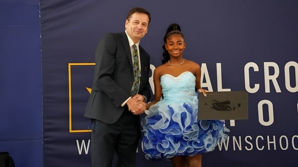 Un hombre y una mujer están frente a un banner con el nombre de la Royal Crown School.