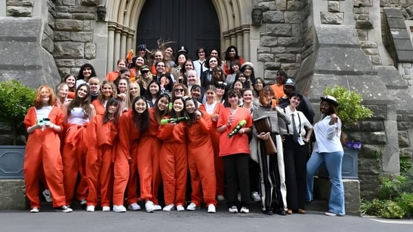 Un gran grupo de estudiantes de la Royal High School está de pie en atuendos rojos frente a un edificio de piedra con una entrada arqueada.