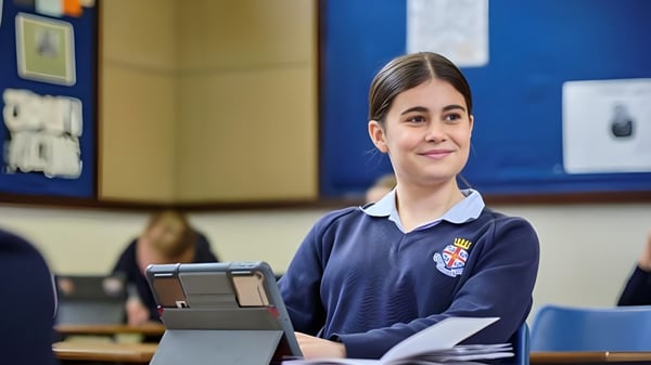 Una alumna de la Royal Hospital School está con uniforme escolar en el aula y sostiene una tablet en la mano.