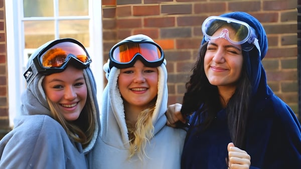 Tres alumnas de la Royal Masonic School for Girls están sonriendo frente a una pared de ladrillos.