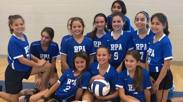 Un grupo de jóvenes atletas en uniformes azules posa juntas en el campo de deportes de la Royal Palm Academy.