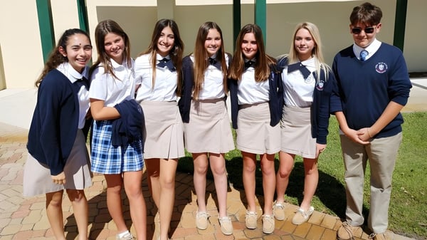 Un grupo de estudiantes de la Royal Palm Academy está afuera frente a un edificio en una plaza pavimentada.