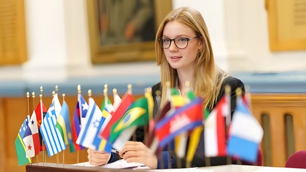Una joven con gafas está frente a una exhibición de banderas internacionales en el terreno de la Royal Russell School.