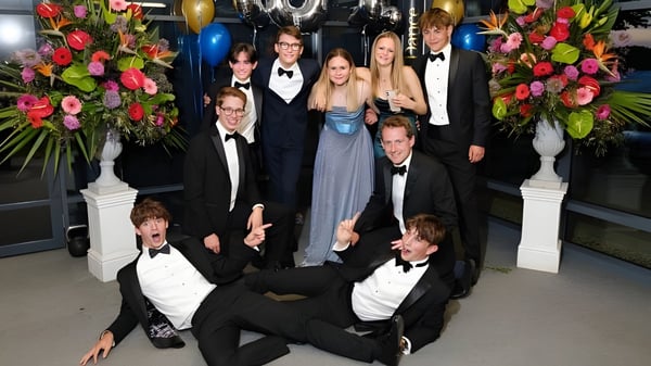 Un grupo de personas vestidas de manera formal posan en un evento con arreglos florales en el campus de la Royal Russell School.