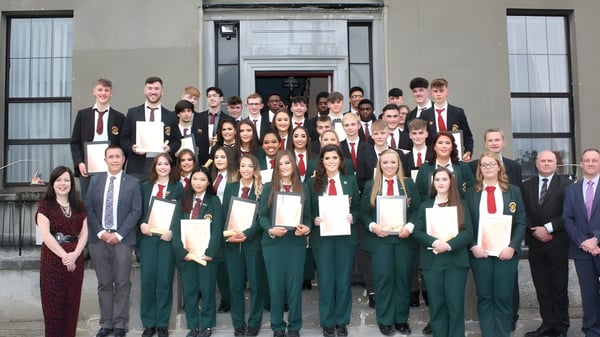 Un gran grupo de estudiantes de la Royal School Cavan está vestido de manera formal frente al distintivo edificio escolar.