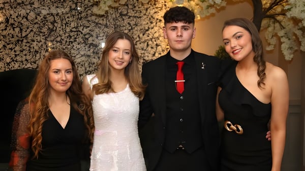 Cuatro estudiantes de la Royal School posan juntos frente a una pared de piedra decorativa.