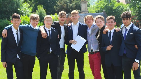Un grupo de jóvenes hombres en ropa formal está en el terreno de The Royal School Wolverhampton frente a una estatua al aire libre.