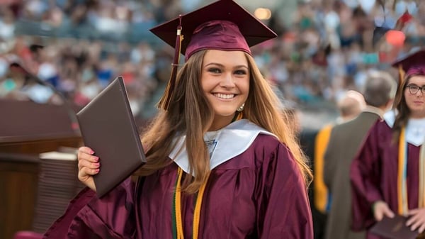Una graduada en toga burdeos está con otros estudiantes en la ceremonia de graduación de la Royal Vale High School al aire libre.