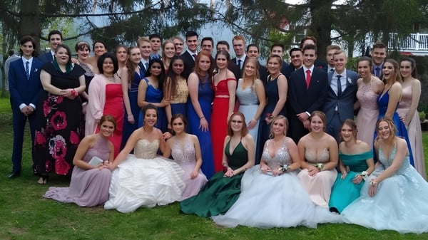 Un gran grupo de estudiantes de Russell High School posan con ropa formal afuera frente a árboles para una foto grupal.