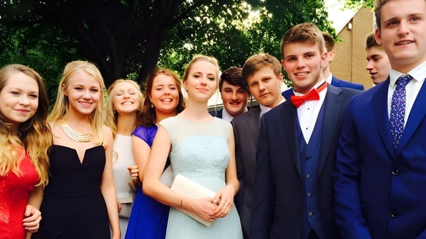 Un grupo de jóvenes de la Ryde School está de pie en ropa formal al aire libre frente a vegetación verde.