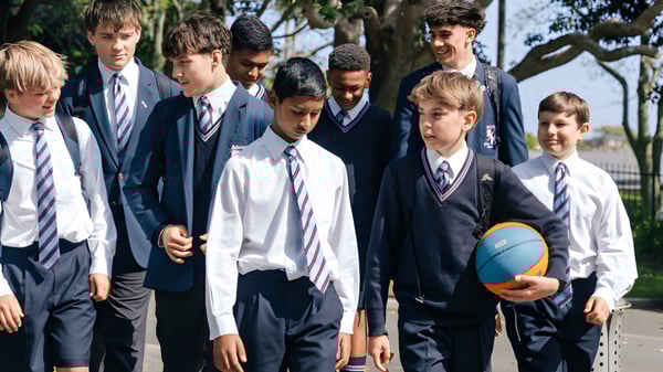 Un grupo de alumnos y alumnas del Sacred Heart College está de pie en uniformes escolares afuera frente a árboles y edificios.