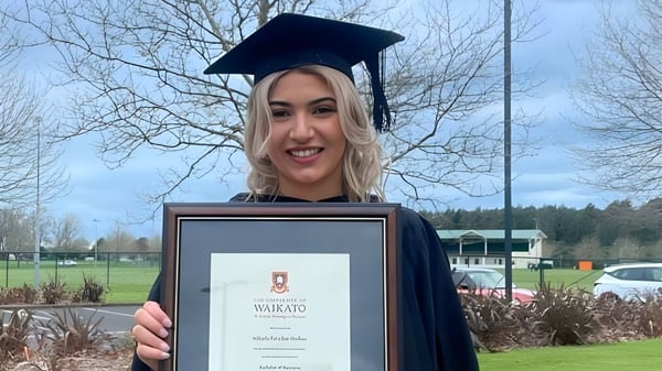 Una graduada sostiene su diploma en el campus del Sacred Heart Girls' College en Hamilton mientras sonríe.