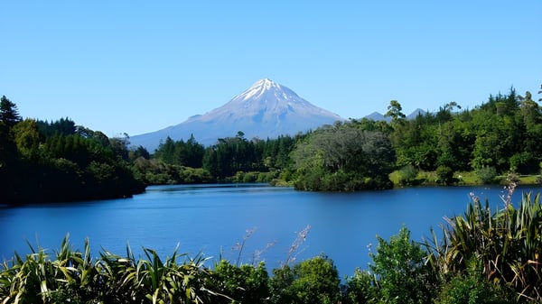 Un lago tranquilo con vegetación ribereña verde y una montaña nevada al fondo cerca del Sacred Heart Girls' College en New Plymouth.