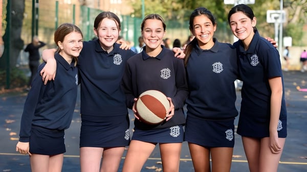 Un grupo de estudiantes de la Sacred Heart High School está con un baloncesto en un área parecida a un parque con árboles y edificios.