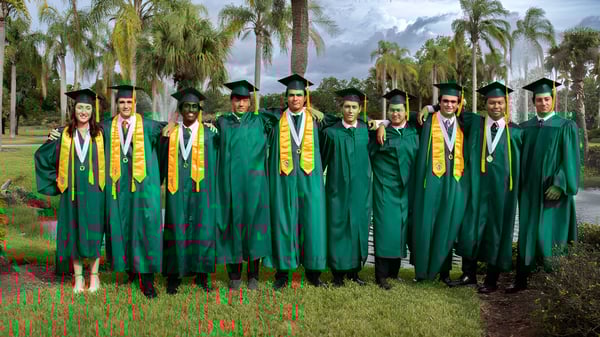 Graduadas y graduados de la Saddlebrook Preparatory School en togas verdes y con estolas amarillas están en el área exterior entre palmeras.