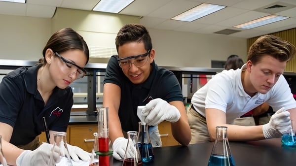 Tres estudiantes de la Sagemont School realizan experimentos científicos en el laboratorio con ropa de protección.