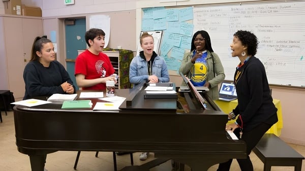 Estudiantes de la Sagemont School se reúnen alrededor de un piano en el aula para una reunión conjunta.