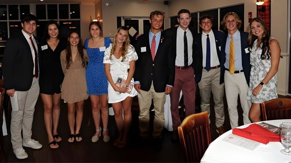 Un grupo de personas se encuentra en un evento de la Saint Andrews School en una sala formal con sofás.