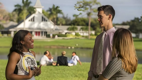 Dos estudiantes de la Saint Andrews School conversan en un prado con una estructura similar a una iglesia en el fondo.