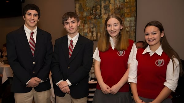 Cuatro estudiantes de la Saint Bernard School están juntos en ropa formal en un entorno escolar.