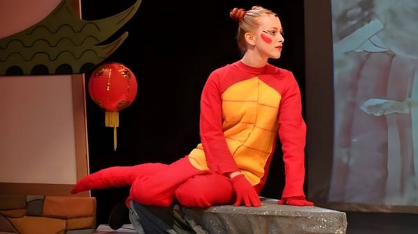 Una persona con disfraz rojo y amarillo está en el escenario de la Saint Edward's School con linternas chinas de fondo.