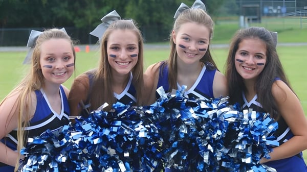 Cuatro alumnas de la Saint Francis Catholic Academy posan al aire libre con pompones azules y blancos como cheerleaders.