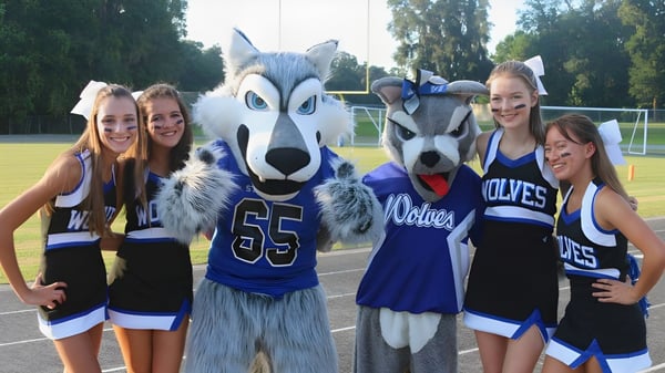 Un grupo de alumnas de la Saint Francis Catholic Academy posan en el campo deportivo con la mascota en uniformes deportivos.