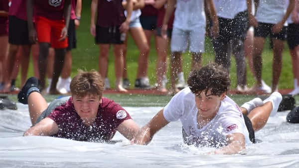 Dos personas están acostadas en un charco de agua frente a una multitud en el terreno de la Saint James School.