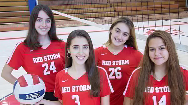 Cuatro estudiantes de la Saint Johns High School llevan camisetas rojas con Red Storm y están juntas en un gimnasio.