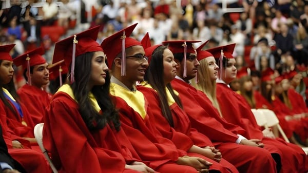 Graduadas y graduados de la Saint Johns High School en togas rojas están sentados en un auditorio durante la ceremonia de graduación.