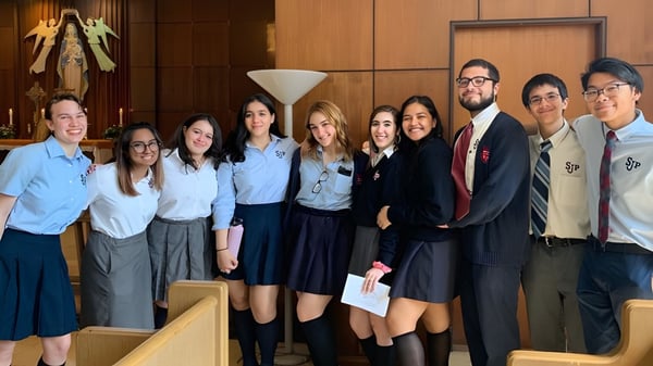 Un grupo de estudiantes posan juntos en una sala con paneles de madera en la Saint Johns High School.