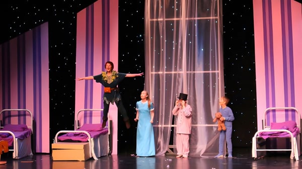 Los estudiantes de Saint John's Prep presentan una actuación escénica con trajes coloridos y un fondo estrellado.