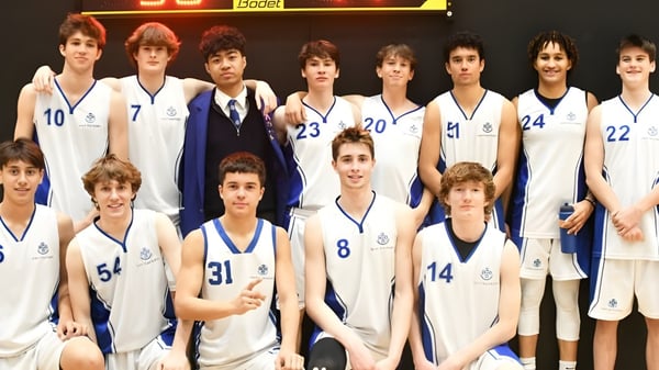 Un grupo de jóvenes jugadores de baloncesto está de pie en uniforme frente al marcador en el campus del Saint Kentigern College.