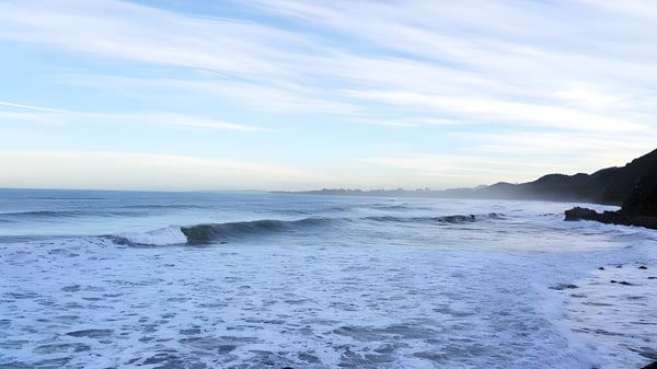 Un tranquilo paisaje costero con olas y una ciudad lejana bajo un cielo nublado cerca del Saint Kentigern College.